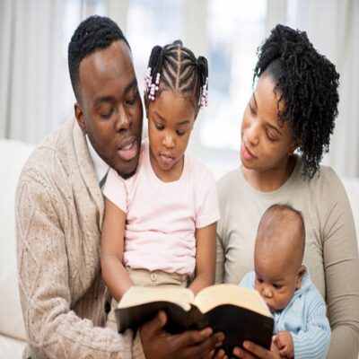 Family spending quality time together in their home living room, reading a book (bible) together.